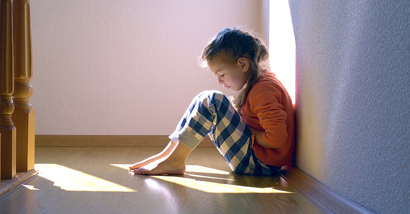 A young child sitting alone, looking down with a sad expression, highlighting the emotional impact of child abuse.