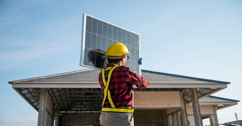 Construction worker safely lifting solar panel