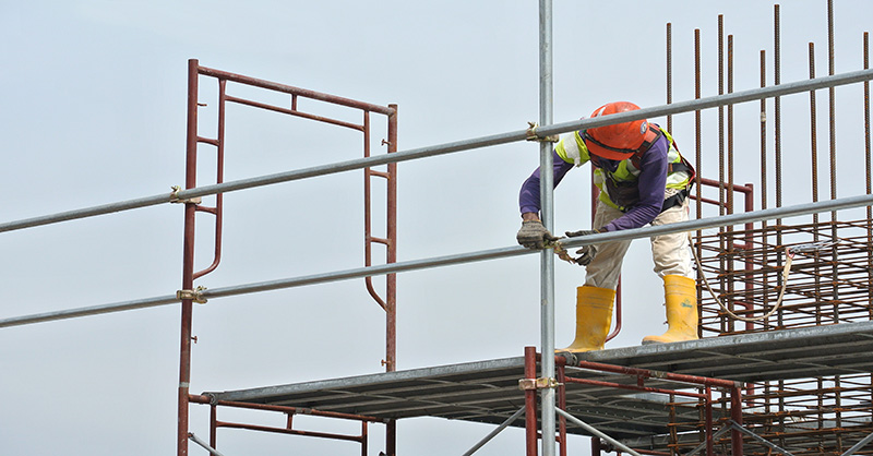 A construction worker working on scaffolding while wearing a safety harness to prevent a fall