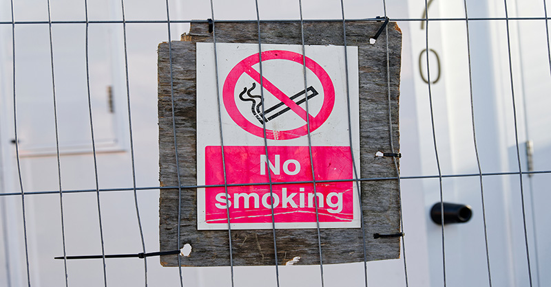 A no smoking sign attached to a fence at a construction site.